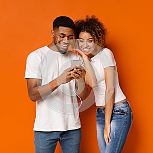 Cheerful african man and woman listening to music on cellphone photo