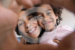 Cheerful African mother and happy daughter looking through hand heart