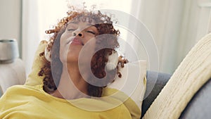 Cheerful african woman using phone and wearing headphones and listening to music while relaxing at home. Happy young