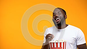 Cheerful Afro-American man eating popcorn and laughing out loud, comedy show