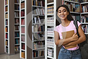 Cheerful afro girl student standing next to bookshelves