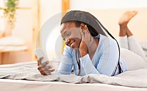 Cheerful Afro Woman Using Smartphone Lying In Bed
