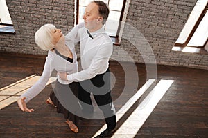 Cheerful aged couple waltzing at the ballroom