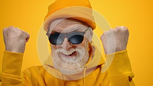 Cheerful aged man enjoying time in studio. Old guy raising hands indoors.