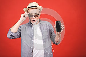 Cheerful aged senior listening to music on a phone isolated against red background