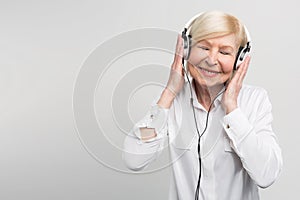 Cheerful aged woman listening to music in headphones. She is enjoying the moment. on white background.