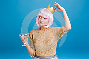 Cheerful amazing young woman with pink haircut having fun on blue background. Golden crown on head, brightful makeup