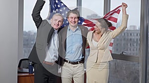 Cheerful American business team posing with national flag in office. Portrait of happy smiling men and woman holding USA