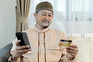 Cheerful arab man with credit card and smart phone shopping online., online shopping on smart phone. E-commerce