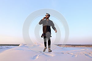 Veselý arabský chlap komunikuje na telefon a linka v střední z široký poušť na světlo 