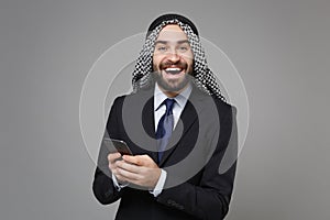 Cheerful arabian muslim businessman in keffiyeh kafiya ring igal agal classic black suit isolated on gray background