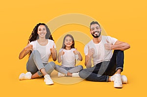Cheerful Arabic Family Gesturing Thumbs Up Approving Something, Yellow Background