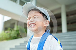 Cheerful Asian boy in backpack and blue cap laughing