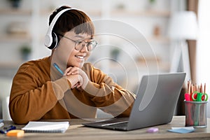 Cheerful asian boy schooler having online lesson from home