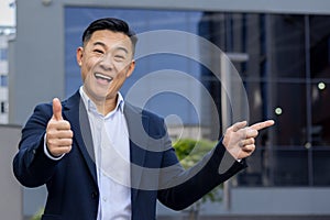 Confident asian businessman giving thumbs up and pointing outside office building