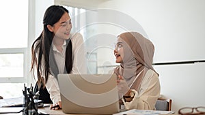 Cheerful Asian businesswoman and her muslim colleague are enjoying sharing their ideas for a project