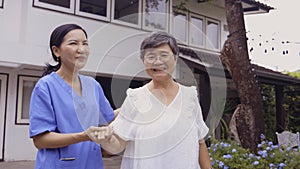 Cheerful Asian caregiver and patient walking outside house