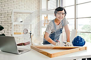 A cheerful Asian carpentry boy wearing safety goggles and work gloves, looking at the camera with construction instruments.