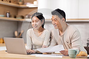 Cheerful asian couple paying bills on Internet, using laptop