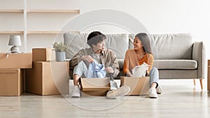 Cheerful Asian couple unpacking belongings and having conversation, moving to new apartment or their own house