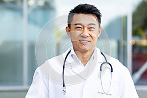 cheerful asian doctor man smiling on the background of a modern clinic outdoors