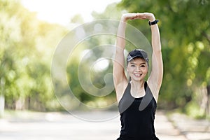 A cheerful Asian female runner in sports outfits doing stretching before jogging exercise outdoor in the city natural park under