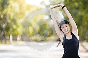 A cheerful Asian female runner in sports outfits doing stretching before jogging exercise outdoor in the city natural park under