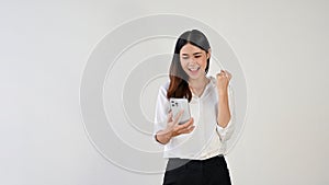 A cheerful Asian female is showing her fist while looking at her smartphone screen