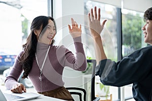 A cheerful Asian female worker gives high fives to a male colleague to cheer up