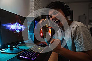 Cheerful asian gamer boy rejoicing victory while playing video g