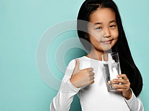 Cheerful asian girl in white longsleeve standing with glass of pure water and showing thumbs up sign