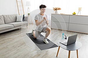 Cheerful Asian guy doing forward lunges in front of laptop