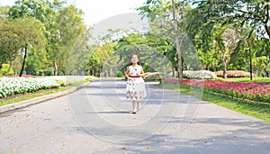 Cheerful asian little girl in white dress running on road in garden