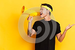 Cheerful Asian man in black t-shirt with, screaming to the megaphone with closed eyes and hand a side, isolated on