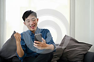 Cheerful Asian man celebrating good news after get an unexpected sms