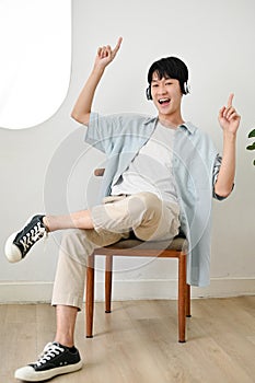 Cheerful Asian man enjoying with the music, listening to music through headphones in living room