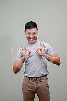 Cheerful Asian man showing OK hand sign while standing against an isolated green background