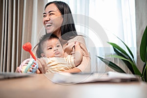 A cheerful Asian mom is laughing and enjoying playing with her baby home in the living room