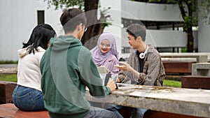 A cheerful Asian-Muslim female college student is doing homework or a group project with her friends