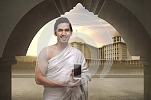 Cheerful asian muslim man with ihram clothes show mobile phone