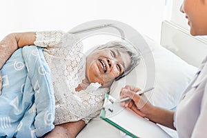 Cheerful Asian nurse talking with elderly patient for monitoring and check up.