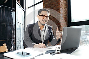 Cheerful asian office worker making video call on laptop smiling and showing thumb up