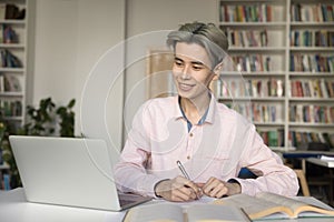 Cheerful Asian teen student studying in university library