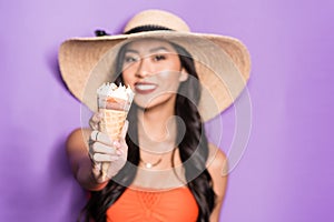 cheerful asian woman in beach attire holding out an ice-cream cone and looking