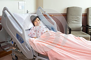 Cheerful Asian woman on bed in hospital ward seeking medical treatment