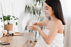 Cheerful asian woman cleaning her face with toner