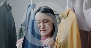 Cheerful Asian woman hanging fashionable clothes on hanger looking at trendy garments smiling at home