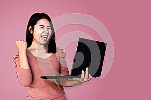 Cheerful Asian woman holding computer celebrating for her success online business concept