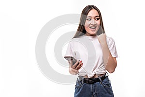Cheerful asian woman holding mobile phone celebrating with win gesture standing isolated over gray background