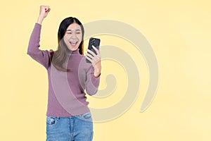 A cheerful Asian woman raises her hand with joy, receiving good news by SMS